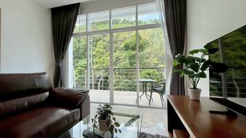 A modern living room with a leather sofa, a glass coffee table, a TV on a wooden stand, and a balcony with a table and chairs.