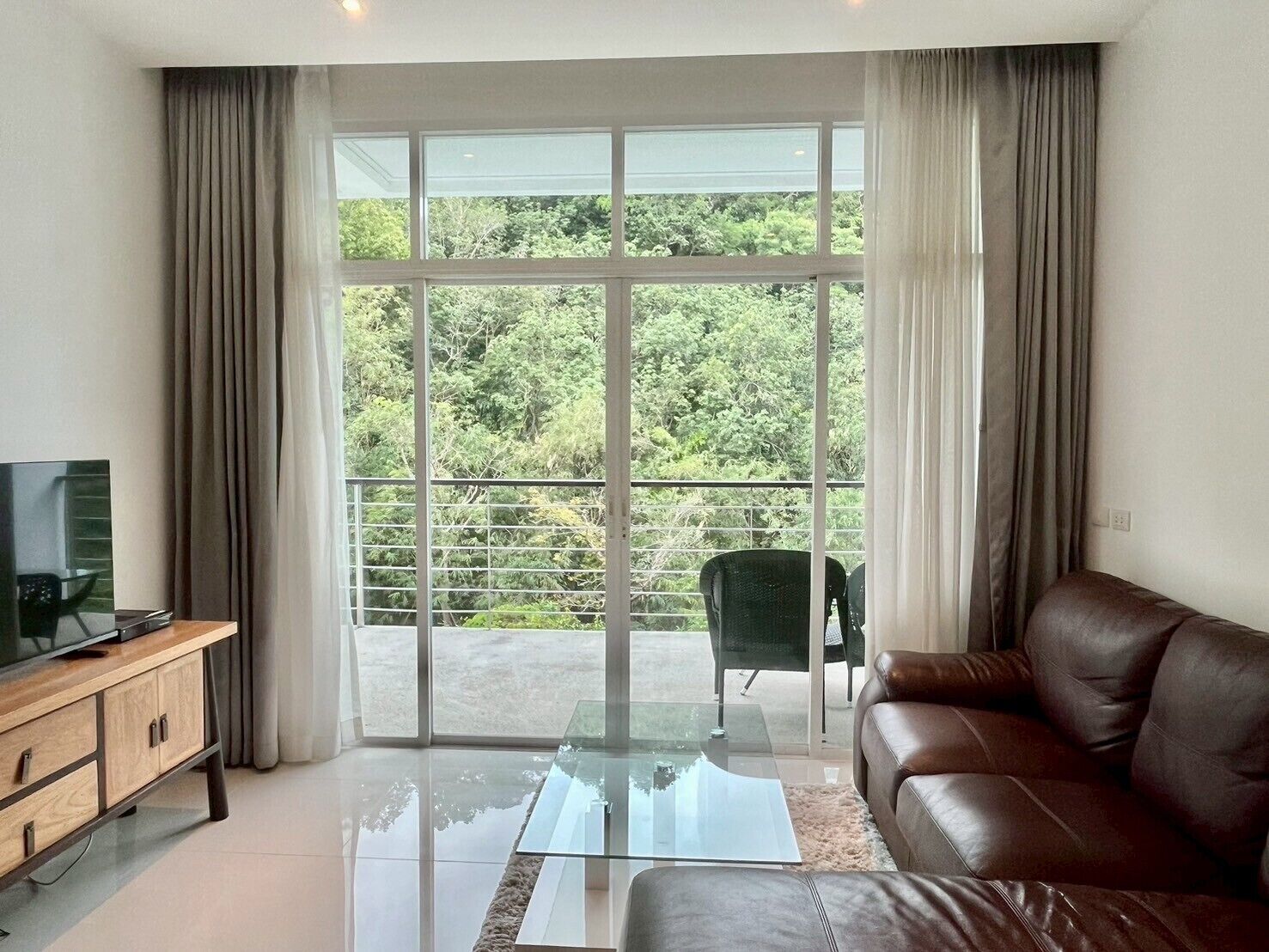 A living room with a glass coffee table, leather sofa, and a TV on a wooden cabinet.