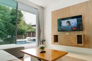 Una sala de estar moderna con un televisor de pantalla plana montado en una pared de madera, una piscina visible a través de amplios ventanales y un área de estar acogedora con una mesa de centro de madera.