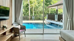 A modern hotel room with a large sliding glass door leading to a private pool, a comfortable seating area, and a flat-screen TV mounted on the wall. - Grand Kamala Falls (Kamala)