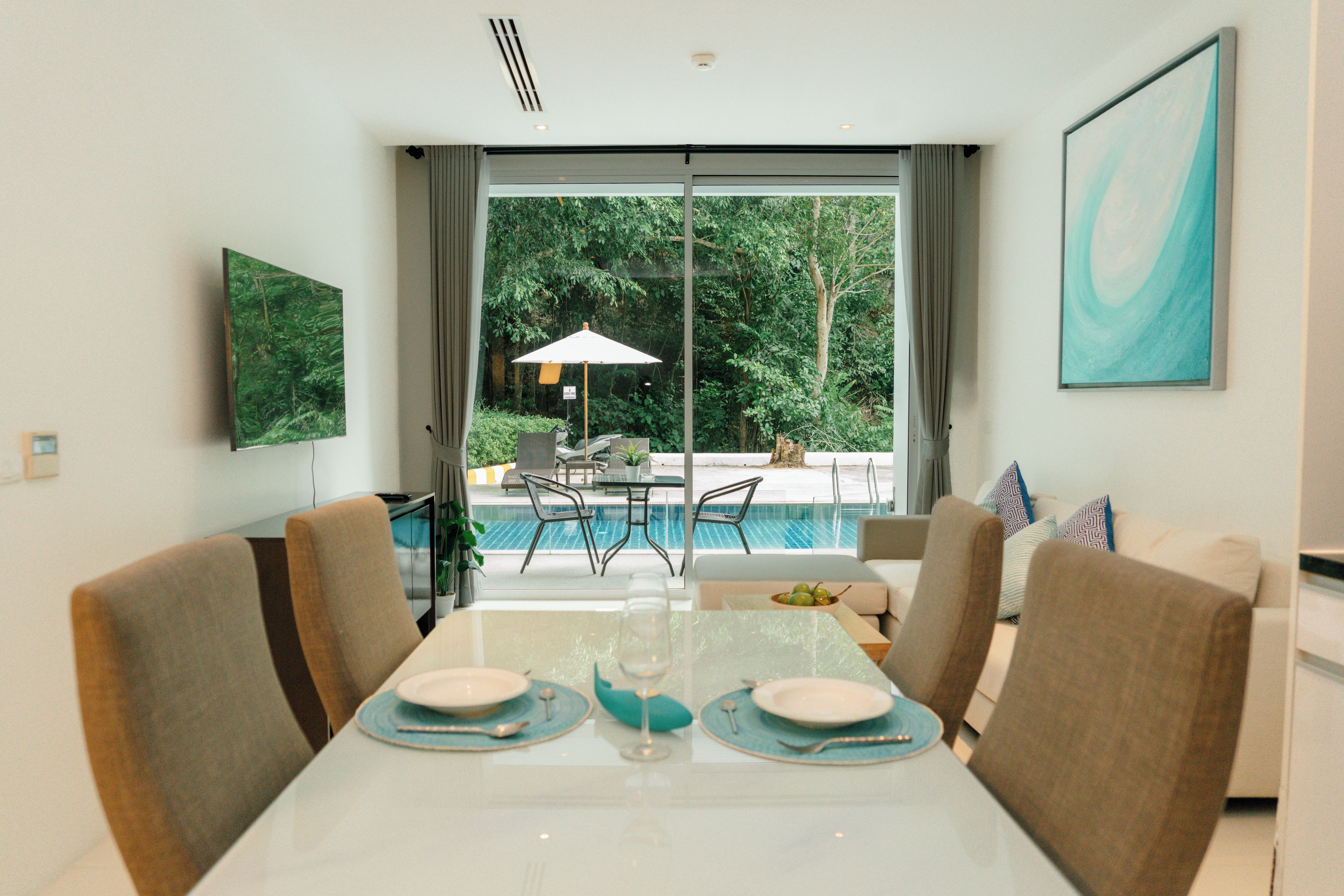 A dining area with a glass table, chairs, and a view of a swimming pool and greenery.