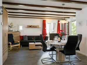 Ein modernes Wohnzimmer mit Essbereich, Holzböden, einer Couch, einem Couchtisch und einem Esstisch für vier Personen.