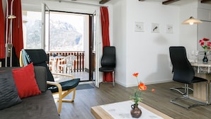Ein modernes Wohnzimmer mit einer Couch, Sesseln, einem Essbereich und Blick auf Berge durch große Fenster.