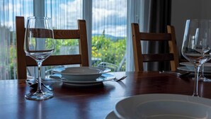 A dining table set with plates, cutlery, and wine glasses, with a view of greenery through large windows. - Saarland by Interhome (Dittishausen)