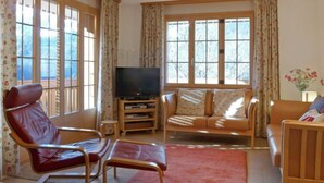 A living room with a TV, leather chairs, a sofa, and large windows. - Panorama Apt. P by Interhome (Wengen)