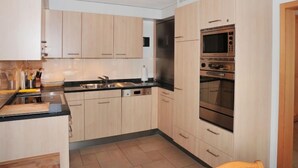 A modern kitchen with light wood cabinets, a black countertop, and stainless steel appliances including a microwave and oven. - Panorama Apt. P by Interhome (Wengen)