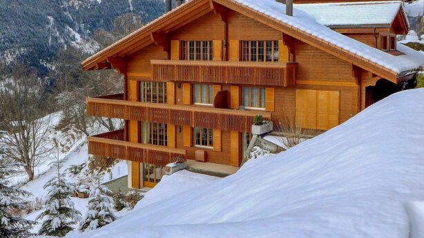 A wooden chalet with multiple balconies and a snow-covered roof, set against a mountainous backdrop. - Panorama Apt. P by Interhome (Wengen)