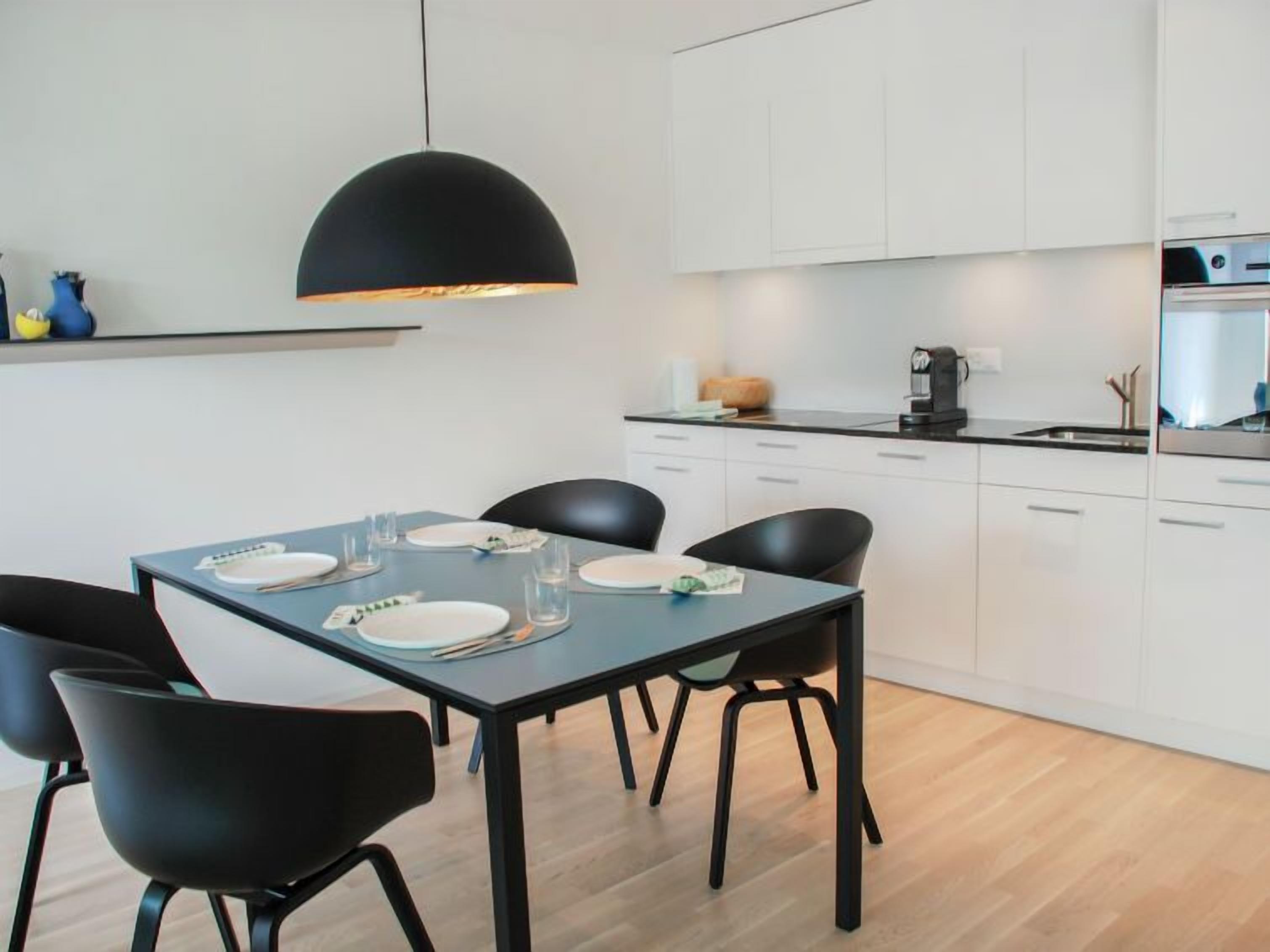 Uma cozinha moderna com armários brancos, uma mesa de jantar preta e cadeiras pretas.