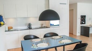 Cocina moderna con armarios blancos, una lámpara colgante negra y una zona de comedor con una mesa azul y sillas negras.