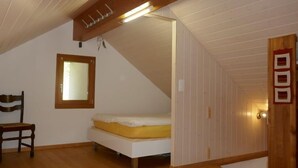 Ett sovrum med en säng, en stol, en trädörr och ett sluttande tak med en lampa.