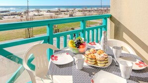 Un balcon avec une table dressée pour deux personnes, donnant sur une plage et l’océan.