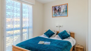 Une chambre à coucher avec un lit, une fenêtre avec des rideaux, une lampe fixée au mur et un tableau.