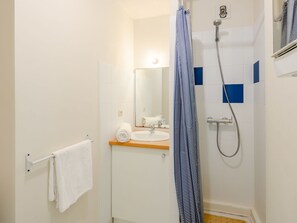 Een badkamer met een wit wastafelmeubel, een spiegel, een douche met een blauw-wit gestreept douchegordijn en een handdoekrek met een witte handdoek.