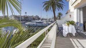 Ein Balkon mit Tisch und Stühlen mit Blick auf einen Yachthafen, wo Boote liegen, und einer Stadtlandschaft im Hintergrund.