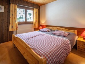 Um quarto aconchegante com uma cama de madeira, duas mesas de cabeceira, uma janela com cortinas e uma luminária na parede.