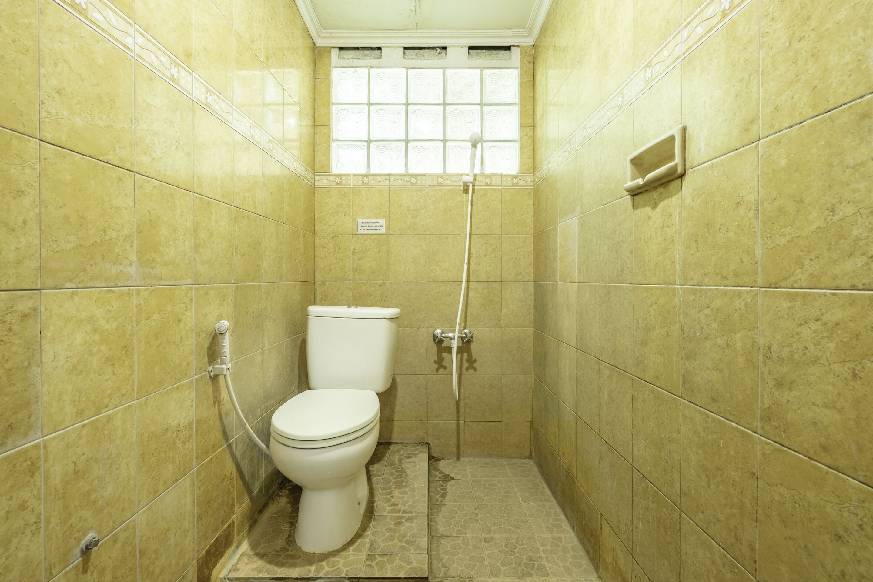 A small, tiled bathroom with a toilet, a shower, and a window.