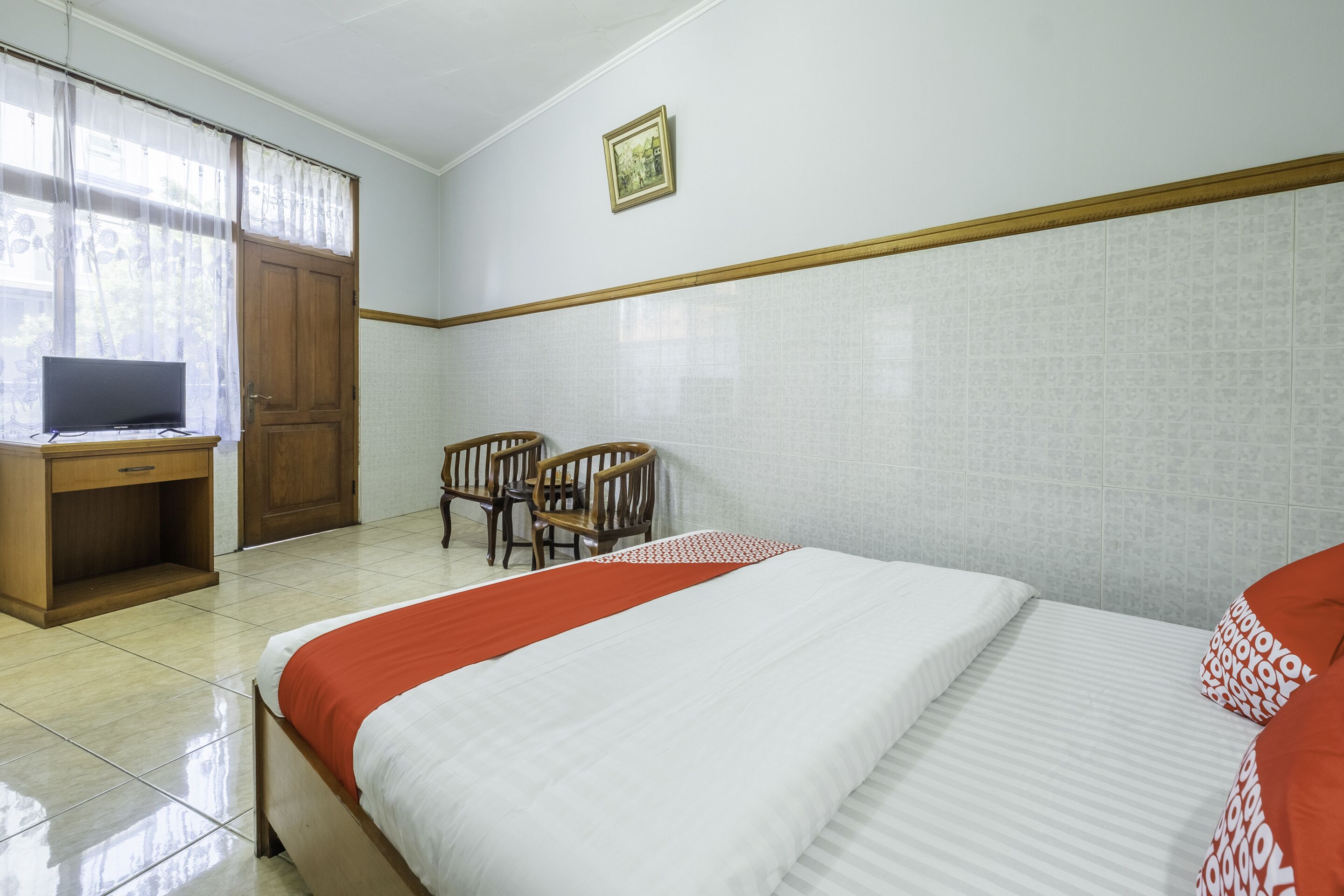 A hotel room with a bed, a desk, two chairs, and a television.