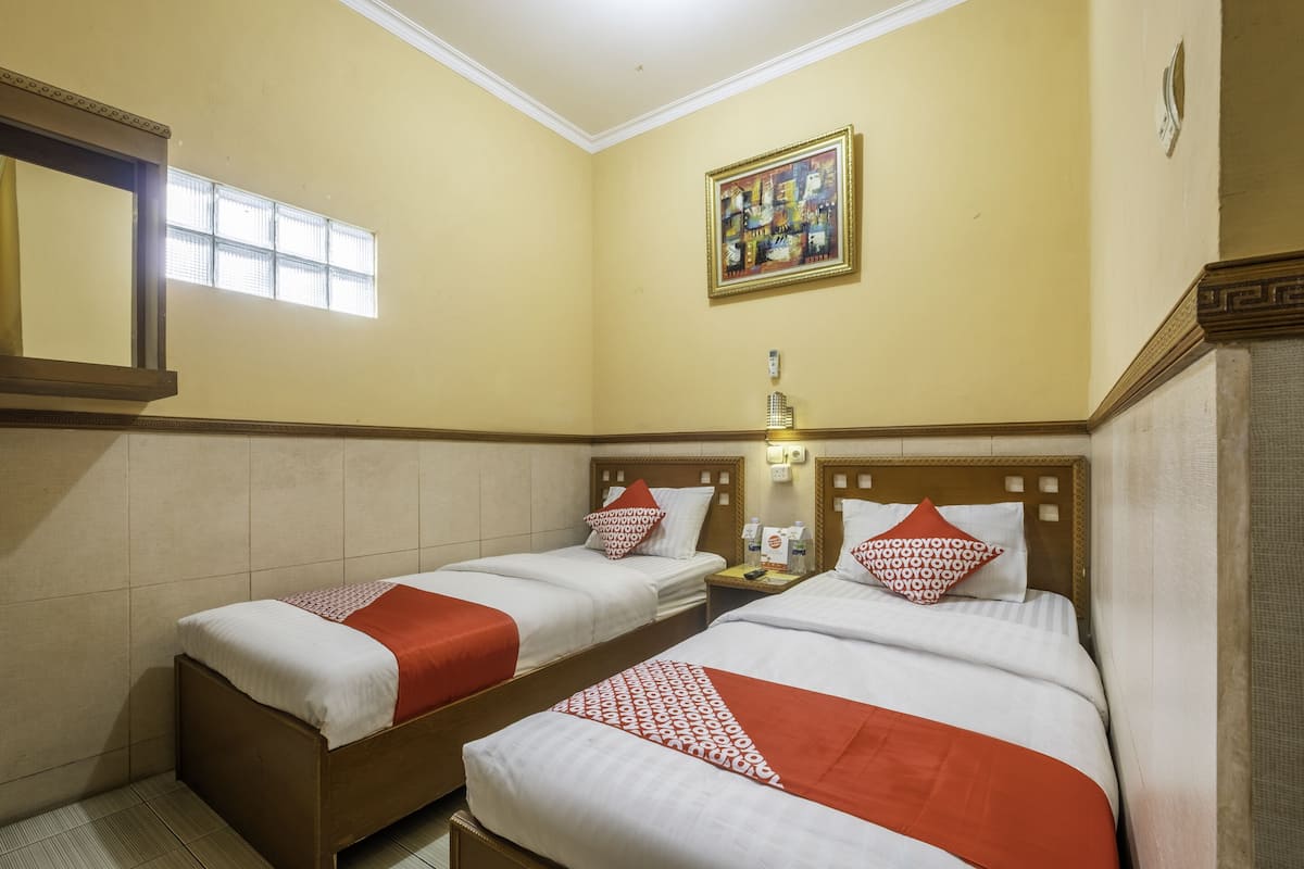 Une chambre d’hôtel avec deux lits simples, chacun recouvert d’une courtepointe rouge et blanche, une table de chevet avec une lampe et un tableau accroché au mur.