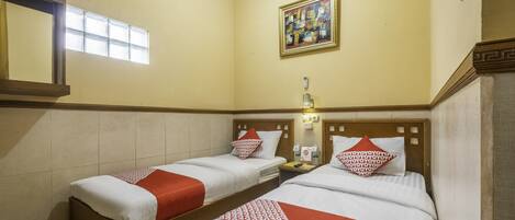 A hotel room with two single beds, each with a red and white bedspread, a nightstand with a lamp, and a painting on the wall.