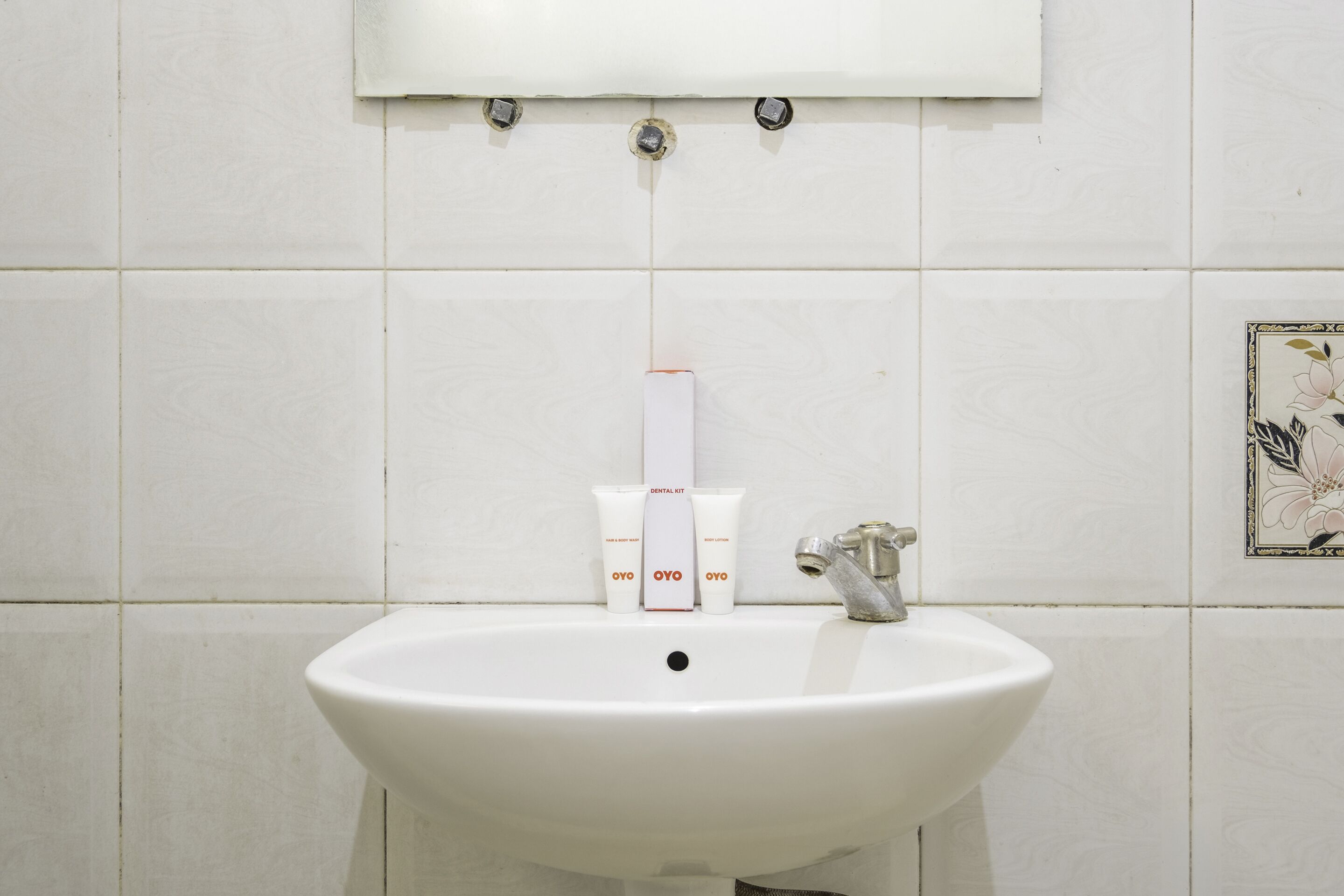 Une salle de bain avec un lavabo blanc, un miroir au-dessus et un porte-rouleau de papier toilette.