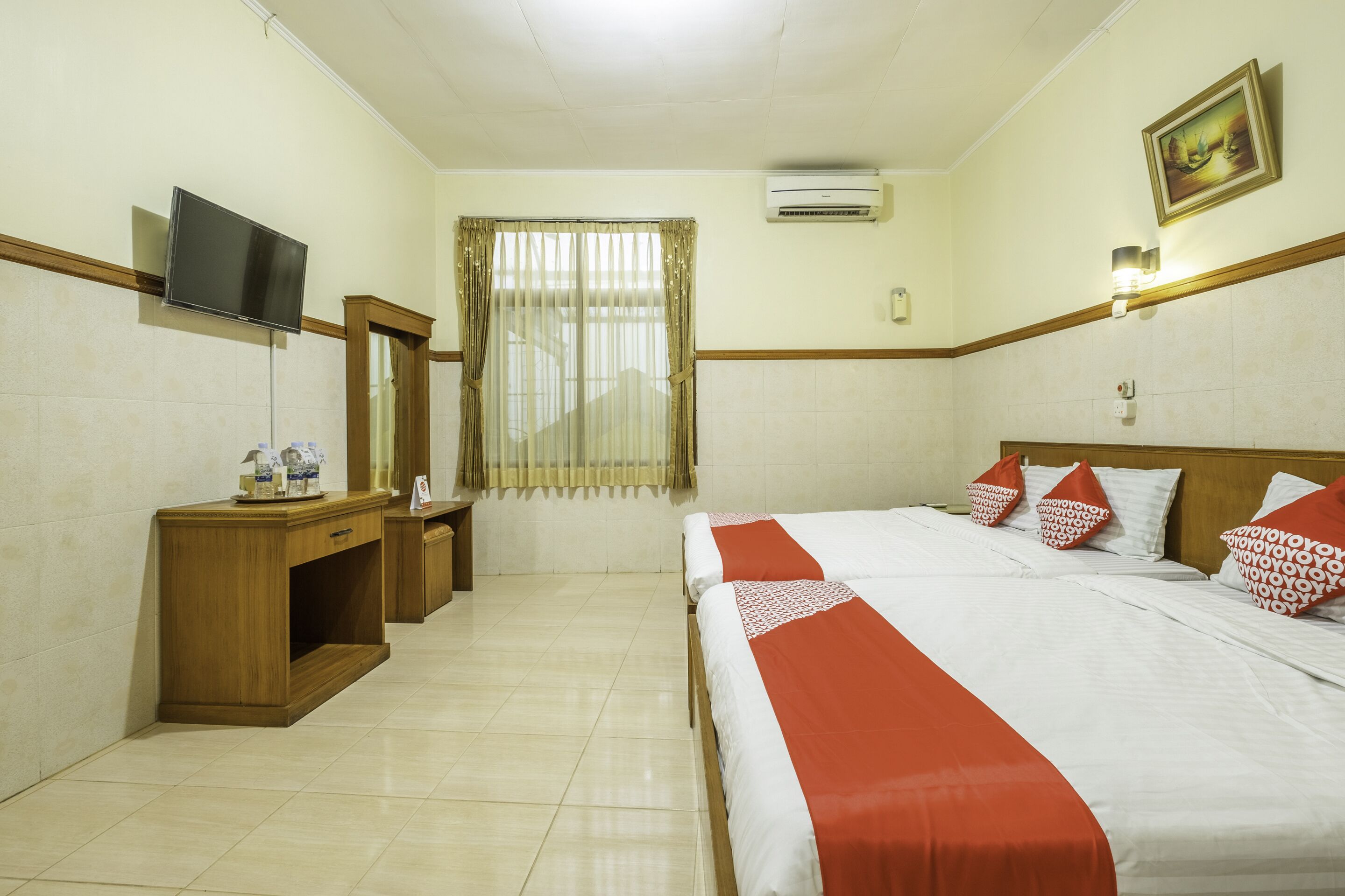 A hotel room with a bed, a TV, a desk, and a window with curtains.
