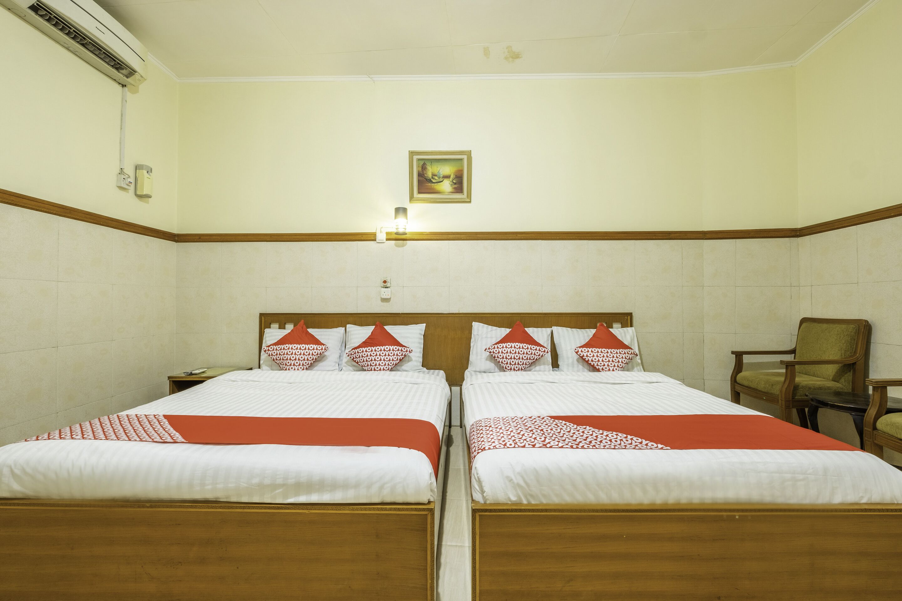 A hotel room with two beds, a wooden headboard, a framed picture on the wall, and a chair.