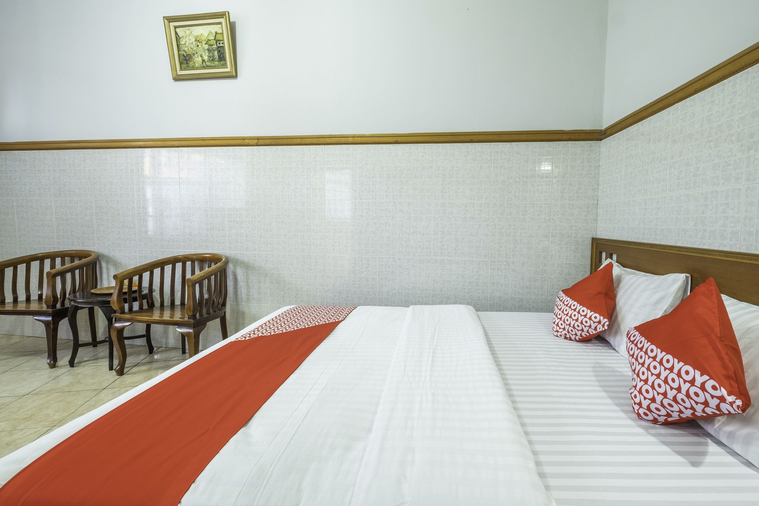 Ein Hotelzimmer mit einem Bett, zwei Holzstühlen, einem kleinen Tisch und einem gerahmten Bild an der Wand.