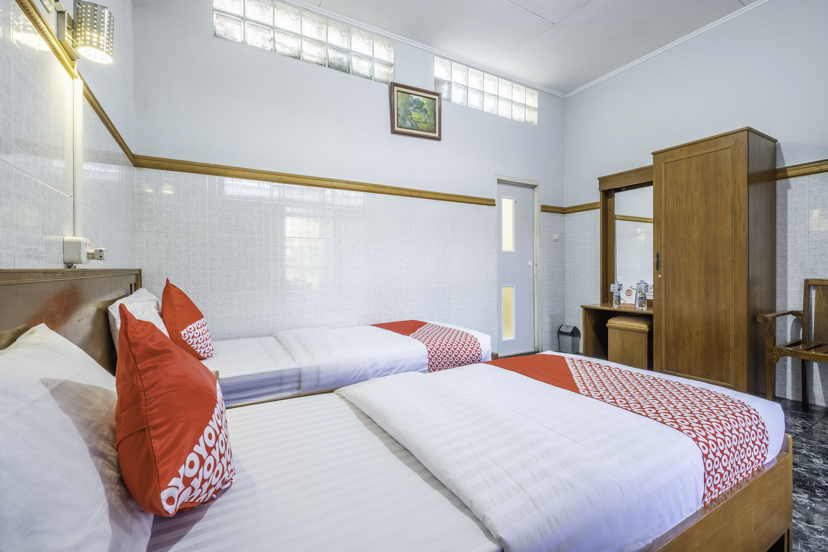 A hotel room with two beds, a wooden wardrobe, a bathroom, and a window with a view.