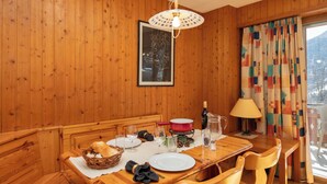 Een houten eettafel met stoelen, een bank, een mand met brood, wijnglazen, een karaf en een fles.