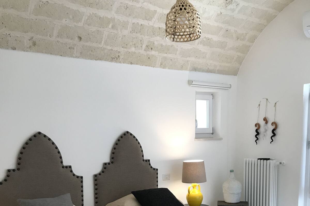 Een slaapkamer met twee bedden, een hanglamp, een klein tafeltje met een lamp en een radiator.