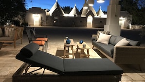 Een buitenterras met rieten meubels, een lounge stoel en een tafel met decoratieve objecten.
