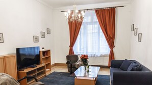 Uma sala de estar com televisão, sofá, poltrona, mesa de centro e uma grande janela com cortinas.