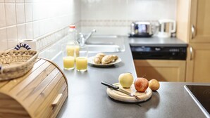 Cozinha com bancada de madeira, tábua de corte com frutas, faca, pia, micro-ondas e cafeteira.