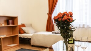 Quarto de hotel com uma cama, uma mesa de cabeceira com um vaso de flores, uma garrafa de vinho e duas taças.
