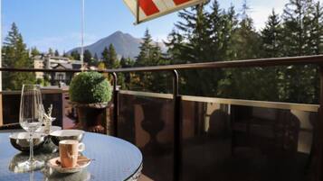 A round table with a glass top, a wine glass, and a cup on a balcony with a red and white striped awning.