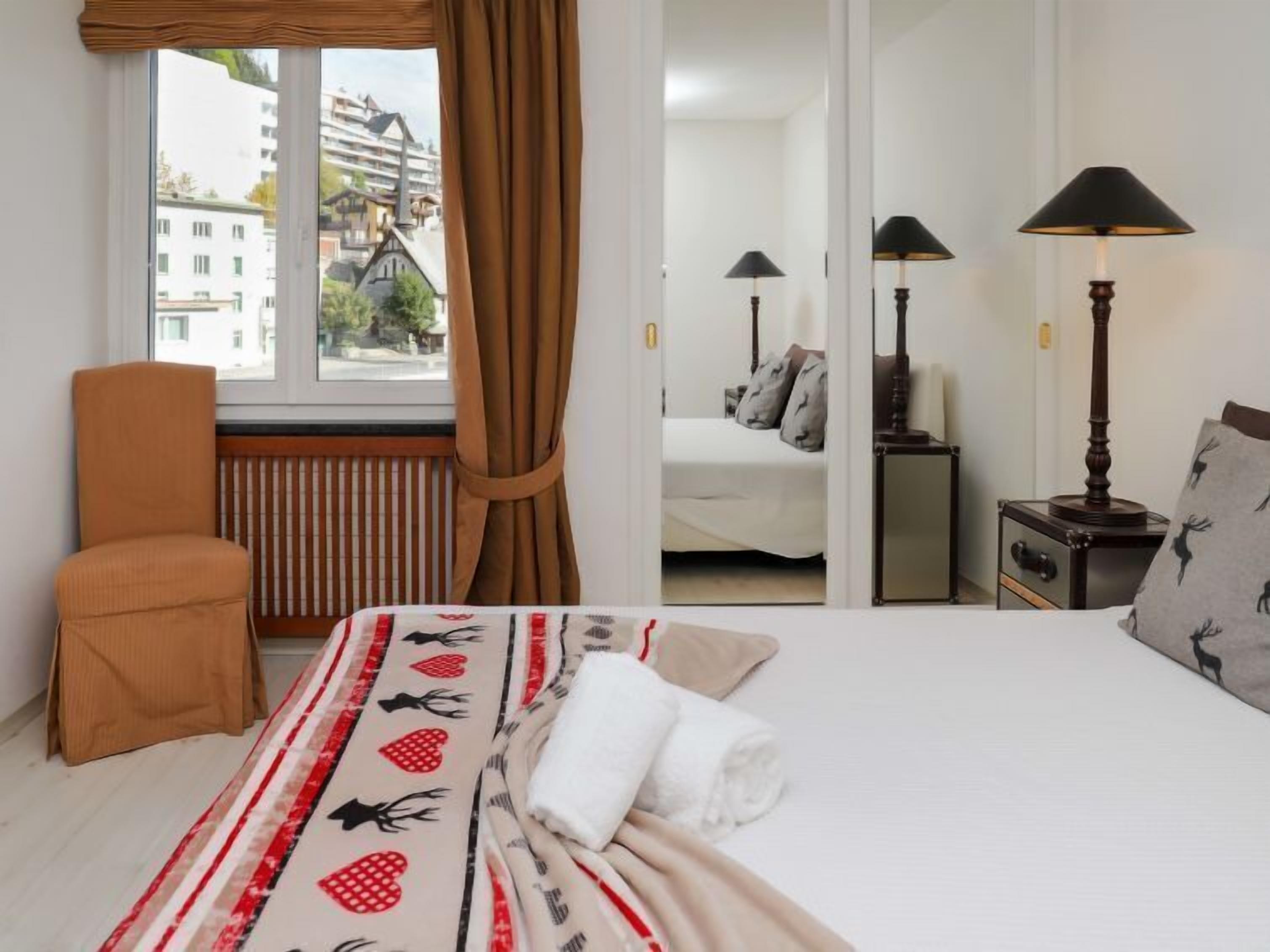 A hotel room with a large bed, a chair, a radiator, a window with curtains, and two bedside lamps.
