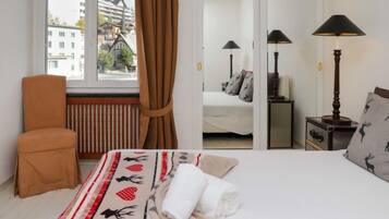 A hotel room with a large bed, a chair, a radiator, a window with curtains, and two bedside lamps.