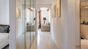 A hallway with a glass partition, a sofa, a chair, and a bed.