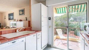 A kitchen with a sink, cabinets, and a view of a balcony with a chair and a grill. - Boulouris Mimosa by Interhome (Saint-Raphaël)