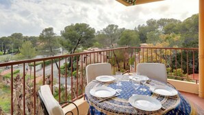 A balcony with a table set for dining, overlooking a scenic landscape with trees and a road. - Boulouris Mimosa by Interhome (Saint-Raphaël)