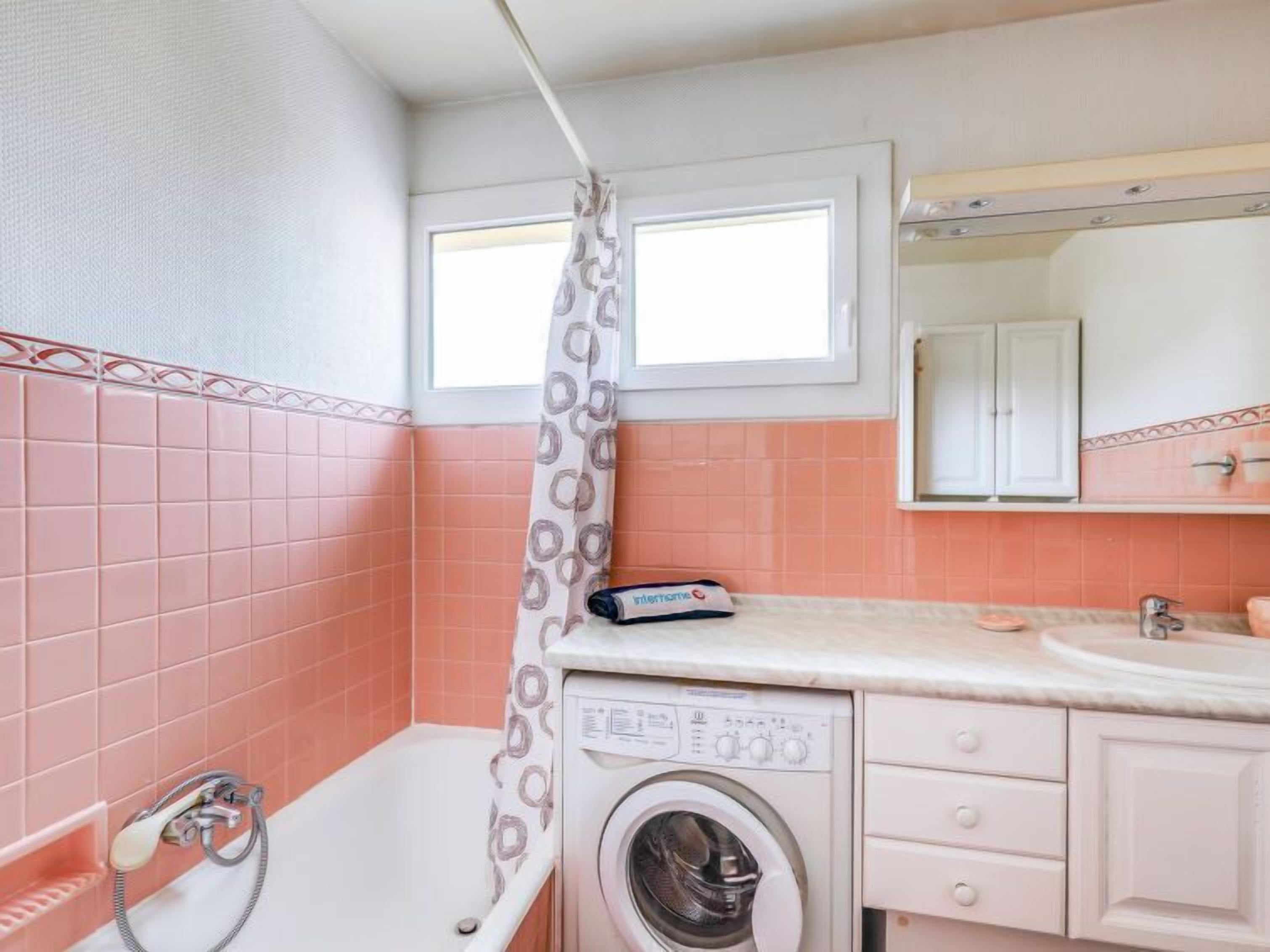 A compact bathroom with a washing machine, a bathtub, and a shower curtain.