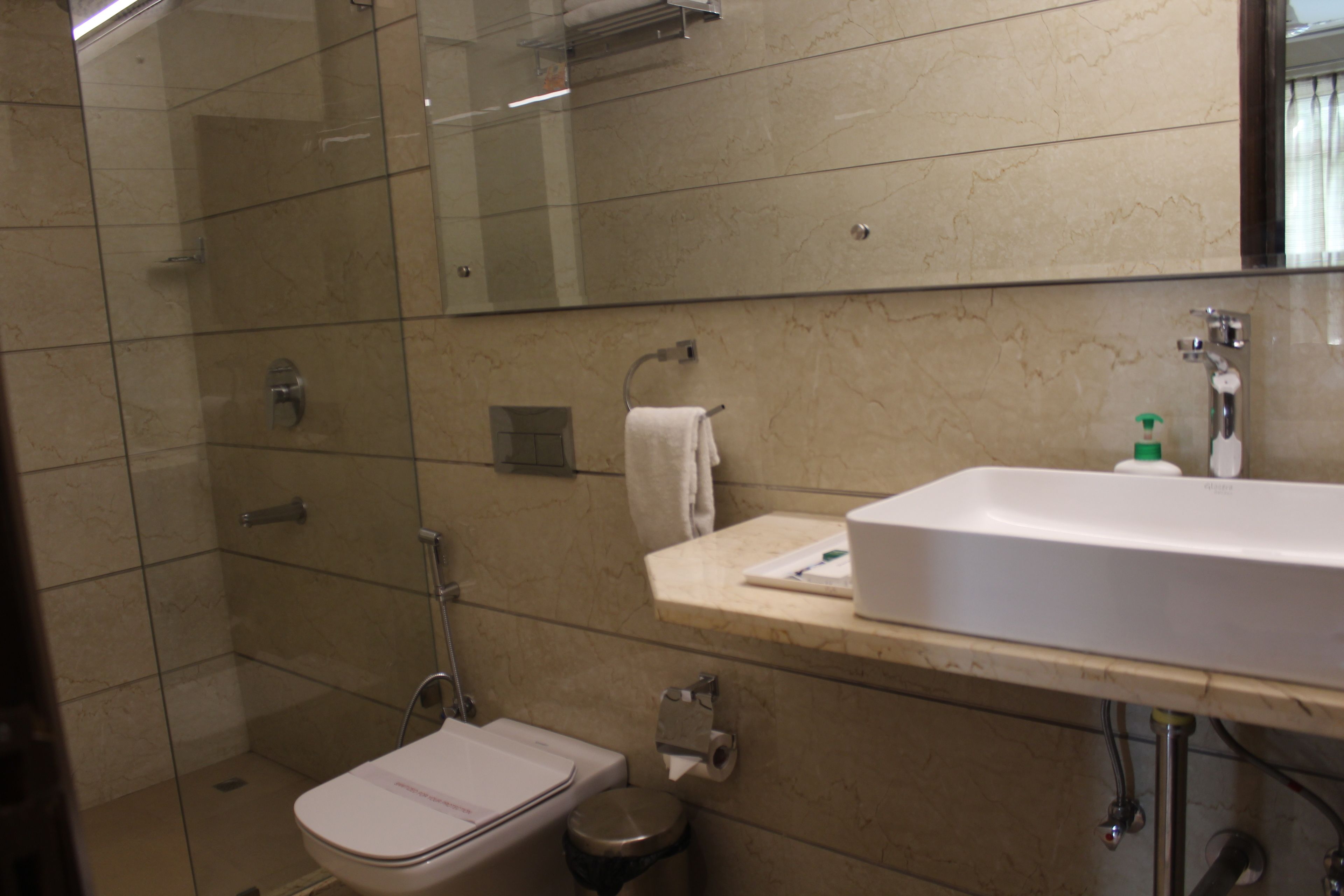 Un baño con cabina de ducha de vidrio, inodoro, lavamanos con espejo y una toalla colgada en la pared.