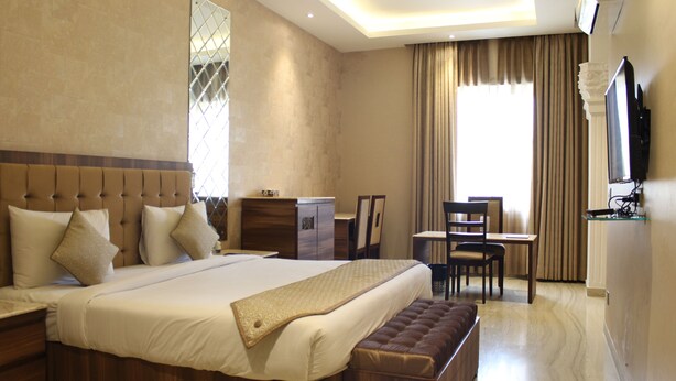 A hotel room with a large bed, a desk, and a television. - Royal Residence Iffco Chowk (Gurugram)