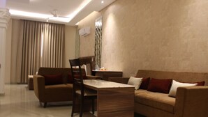 A modern living room with a brown sofa, a wooden coffee table, and a dining area with chairs. - Royal Residence Iffco Chowk (Gurugram)