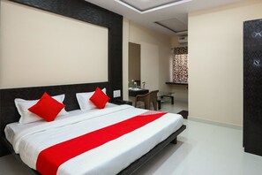 A hotel room with a large bed, a desk, a chair, and a mirror.