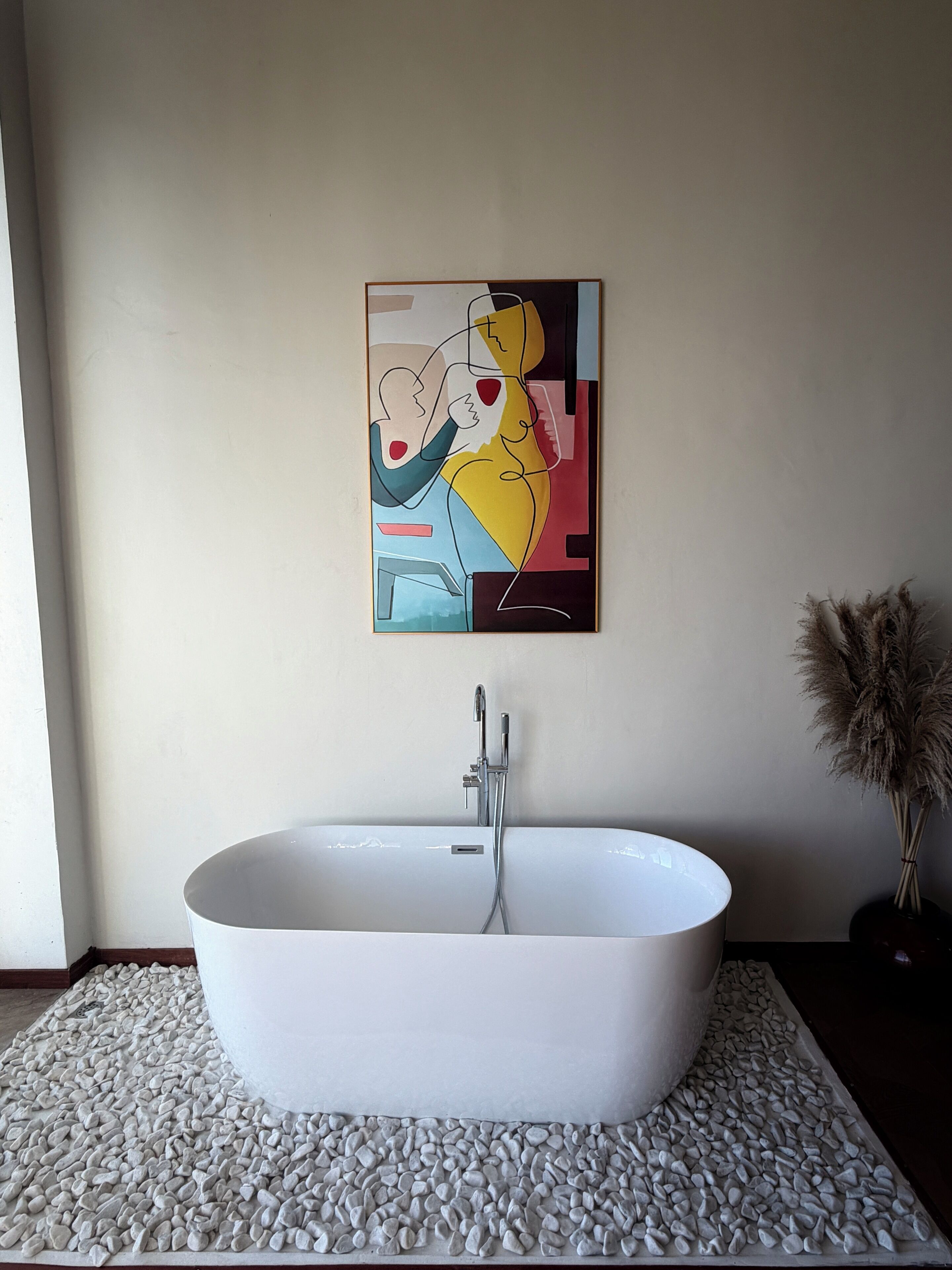 A modern bathroom with a freestanding bathtub, a wall-mounted artwork, and a decorative plant.