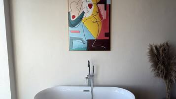 A modern bathroom with a freestanding bathtub, a wall-mounted artwork, and a decorative plant.