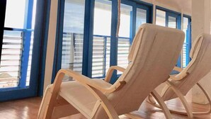 A room with two rocking chairs, a rope hanging from the ceiling, and large windows with blue frames.