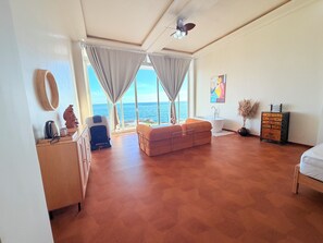 A spacious room with a large window, a ceiling fan, a sofa, a bed, and a wooden dresser.