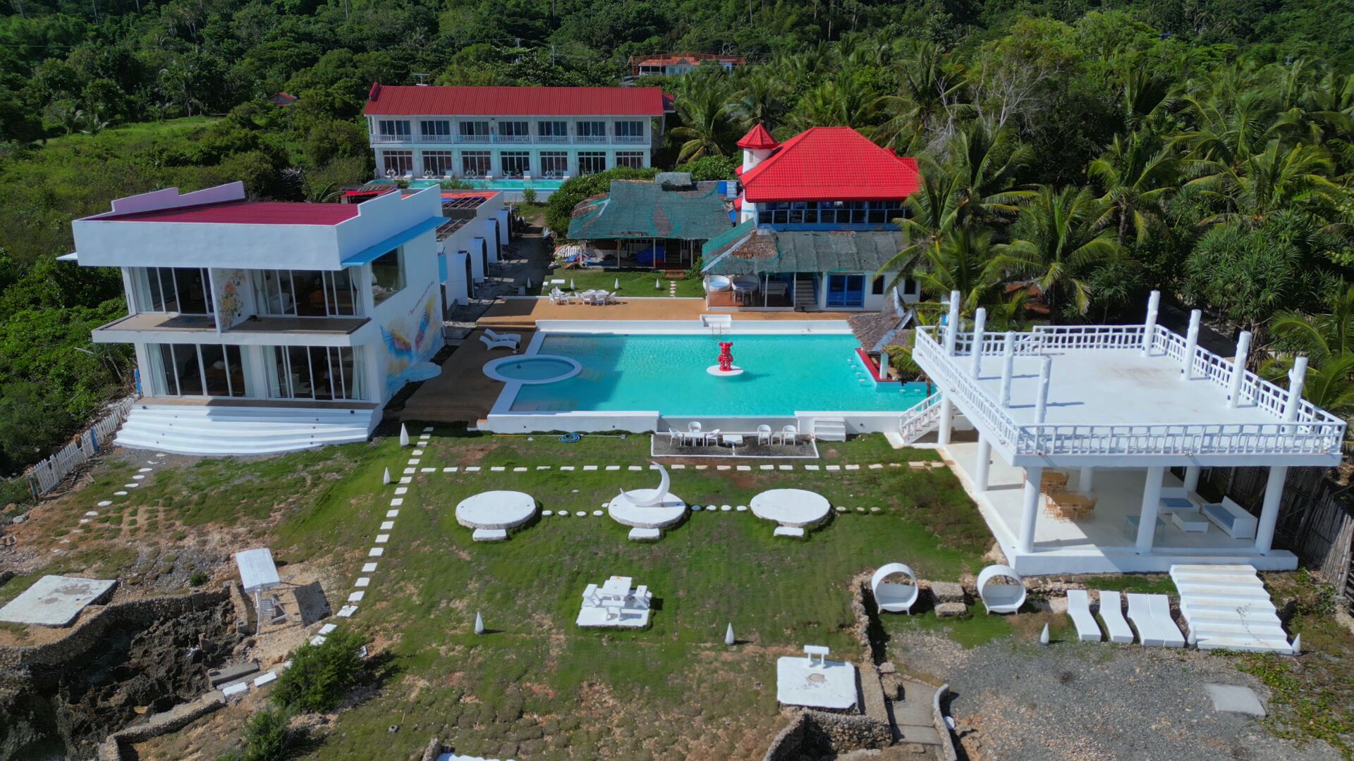 A resort with a swimming pool, multiple buildings, and lush greenery.